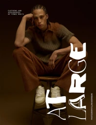 Model with braided hair seated on a wooden stool wearing a brown knit polo shirt and trousers for At Large Magazine cover.