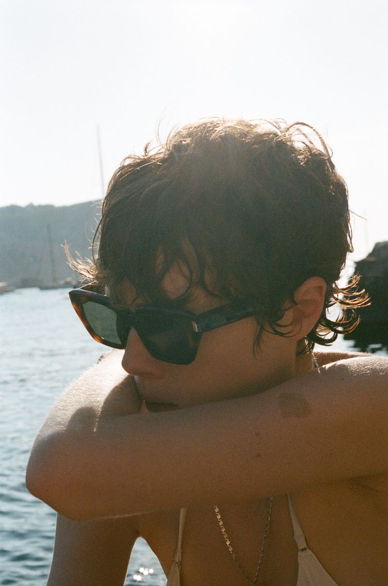 Close-up portrait of model Annabelle Weatherly wearing tortoiseshell sunglasses against an ocean backdrop
