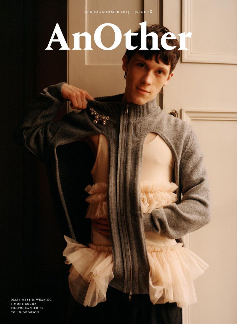 Magazine cover featuring a stylish adult male model wearing a gray cardigan and a ruffled tulle skirt-like garment. Close-up shot.