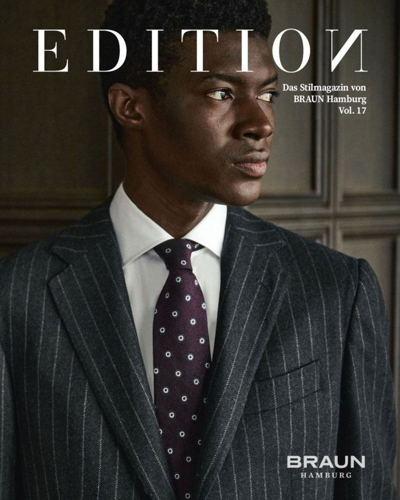 Magazine cover featuring a well-dressed Black man in a pinstripe suit and tie, styled for a fashion editorial, indoors.