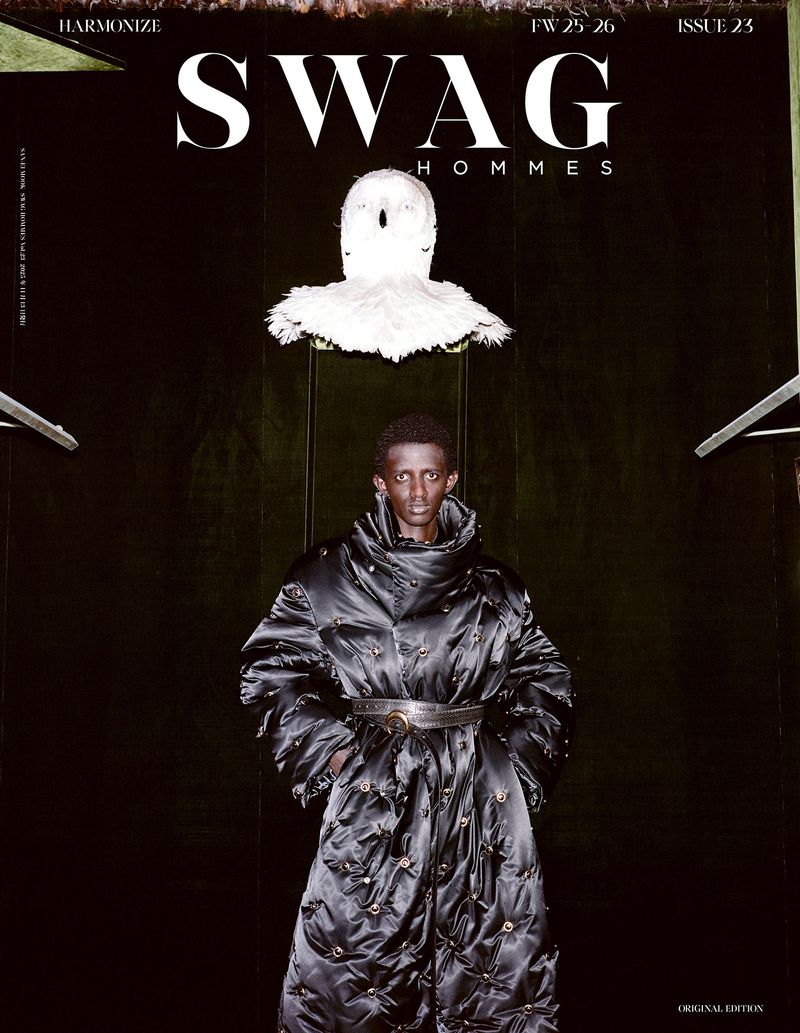 Editorial fashion shot of a Black man in a quilted black coat against a dark background, featured on the cover of SWAG Hommes magazine.
