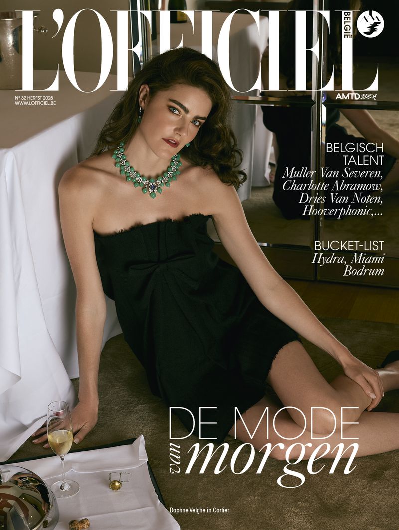 Magazine cover featuring a woman in a black dress and emerald necklace, laying next to a table with a champagne glass and jewelry.