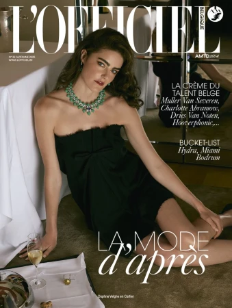 L'Officiel Belgium cover featuring a model wearing a black strapless dress and emerald necklace, seated next to a table with champagne.
