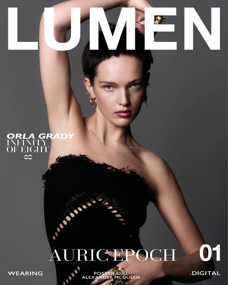 Magazine cover featuring a young woman in a black one-shoulder dress with her arm raised, accessorized with gold earrings and rings, and set against a gray backdrop.