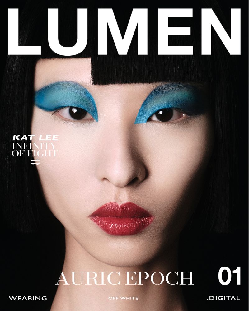 Close-up magazine cover featuring a woman with short black hair, turquoise eyeshadow, and red lipstick against a black background.
