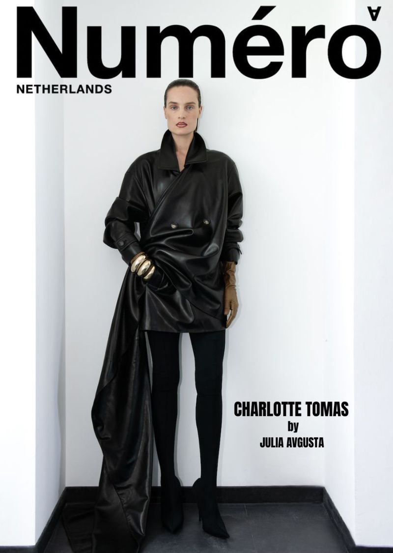 Magazine cover featuring a woman in a black leather coat, black leggings, and black boots, posing against a white wall and black floor.