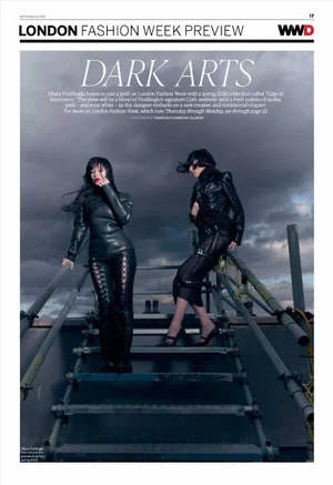 Two women posing on metal rooftop scaffolding in black leather gothic outfits against an overcast cloudy sky.