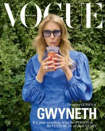 Gwyneth Paltrow wearing a vibrant blue puff-sleeve dress and tinted glasses while holding an iced drink in front of green foliage.