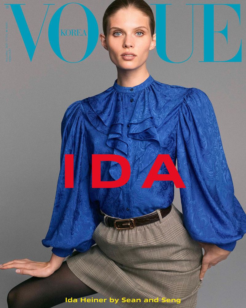 Vogue Korea cover features an adult female model in a blue ruffled blouse, grey plaid skirt, and black tights against a grey backdrop.