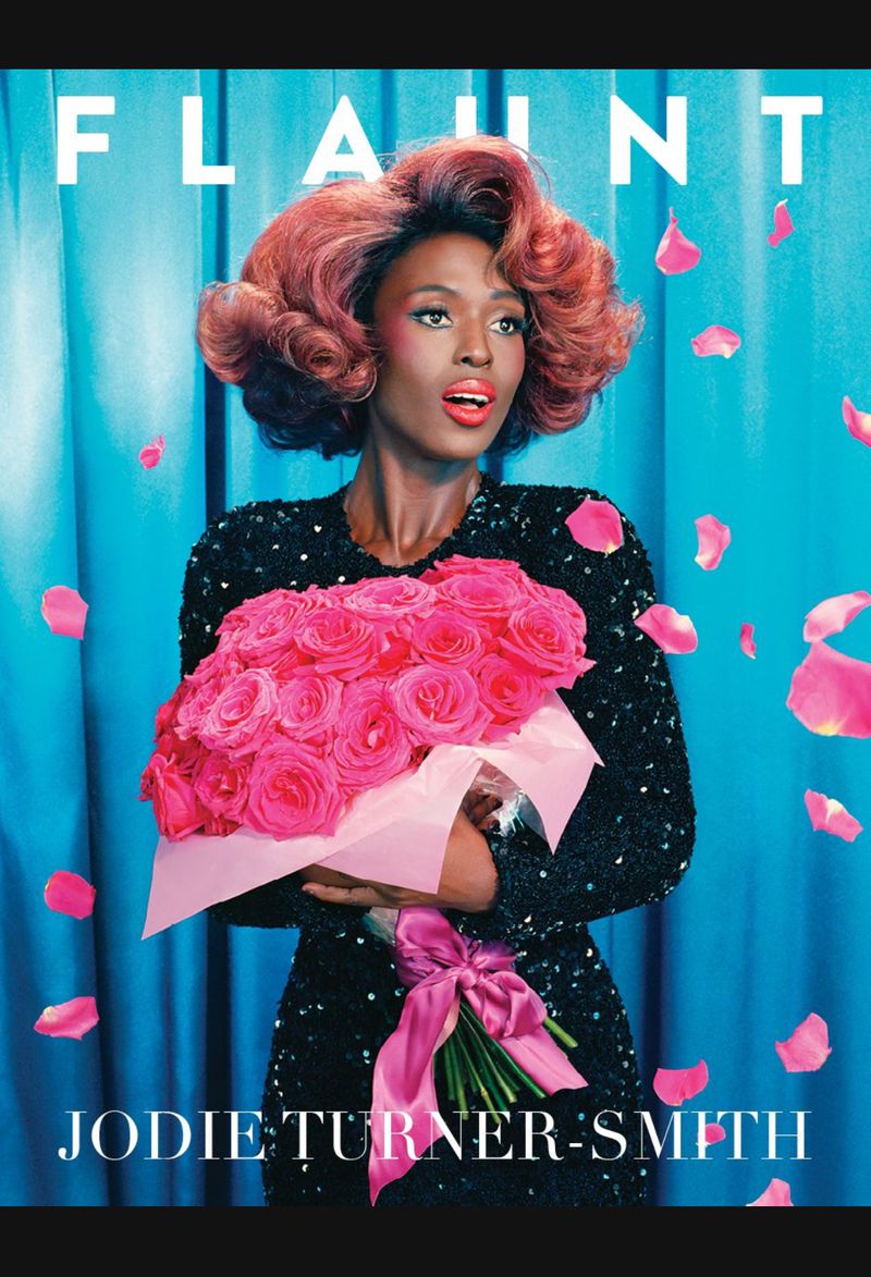 Fashion editorial cover with Jodie Turner-Smith holding pink roses, sparkling black dress, and copper-red curly hair against a blue backdrop.