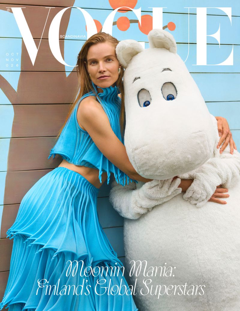Vogue cover featuring a model in a blue dress embracing a Moomin character, against a muted backdrop with a pop of orange.
