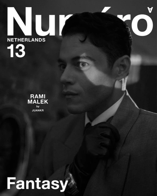 Black and white portrait of Rami Malek for Numero Netherlands magazine cover. He wears a suit, tie, and black gloves, looking off-camera.