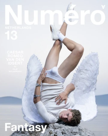 Magazine cover featuring a male model in white underwear, angel wings, and sneakers, inverting on rocks by the water with magazine text.