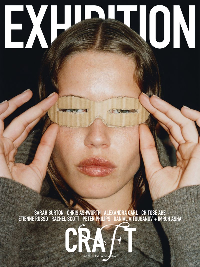 Close-up of woman holding up a cardboard mask to her eyes with the word "EXHIBITION" above her head.
