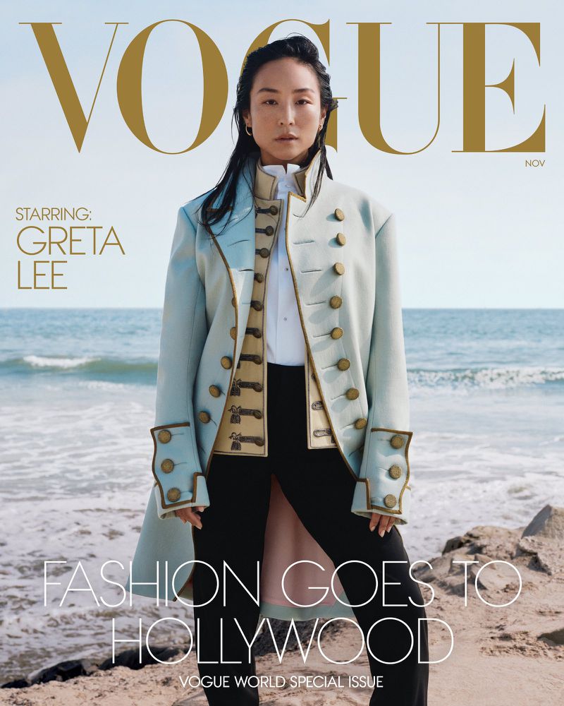 An Asian woman in a light blue military-style jacket stands on a sandy beach with the ocean in the background, appearing on a magazine cover.