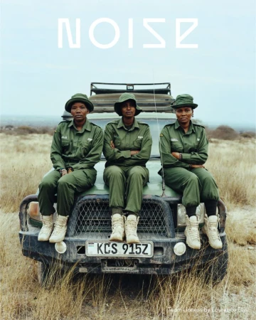 Three women in green uniforms and hats are sitting on the hood of a car. They are in a grassy, outdoor area with a clear, light blue sky.