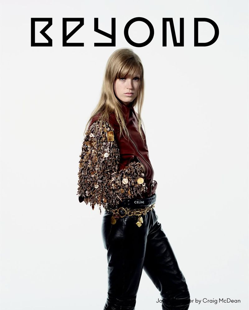 Fashion editorial shot of a woman in a leather jacket with embellished sleeves and leather pants, posing against a bright white backdrop.