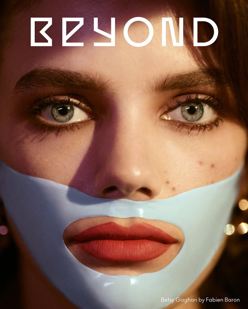 Close-up of a young woman with blue eyes and red lipstick wearing a light blue face mask, emphasizing beauty and skincare in a studio setting.