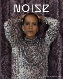 Mati Diop wearing an embellished metallic silver dress with hands raised against damask curtains for Beyond Noise magazine cover.