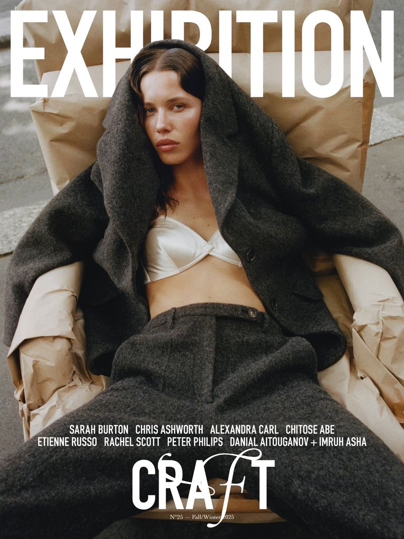 Editorial fashion shot of a model in a wool jacket and pants, posing in a chair with natural makeup and a white bra top.