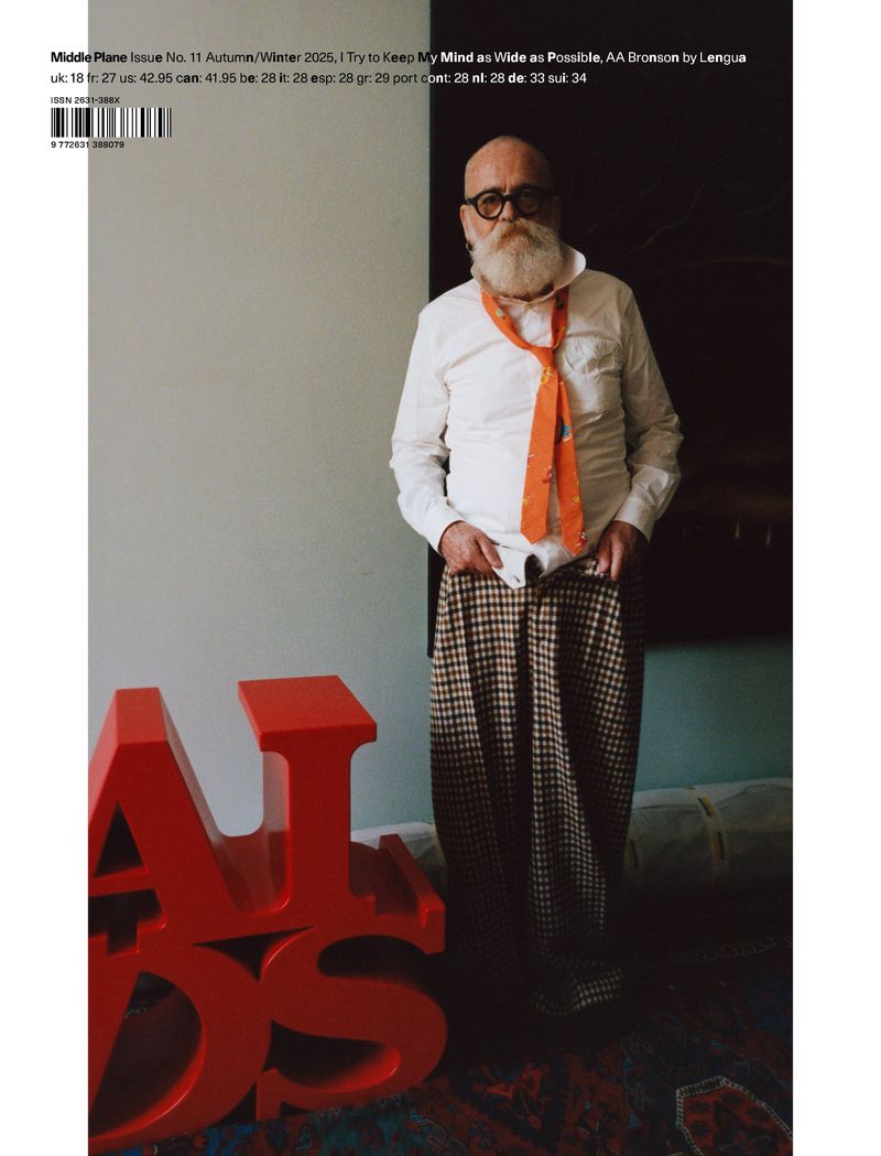 Magazine cover featuring an elderly man with a white beard wearing an orange tie and plaid pants, standing near red 3D letters.