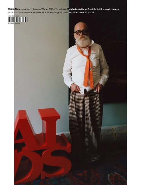 Magazine cover featuring an elderly man with a white beard wearing an orange tie and plaid pants, standing near red 3D letters.