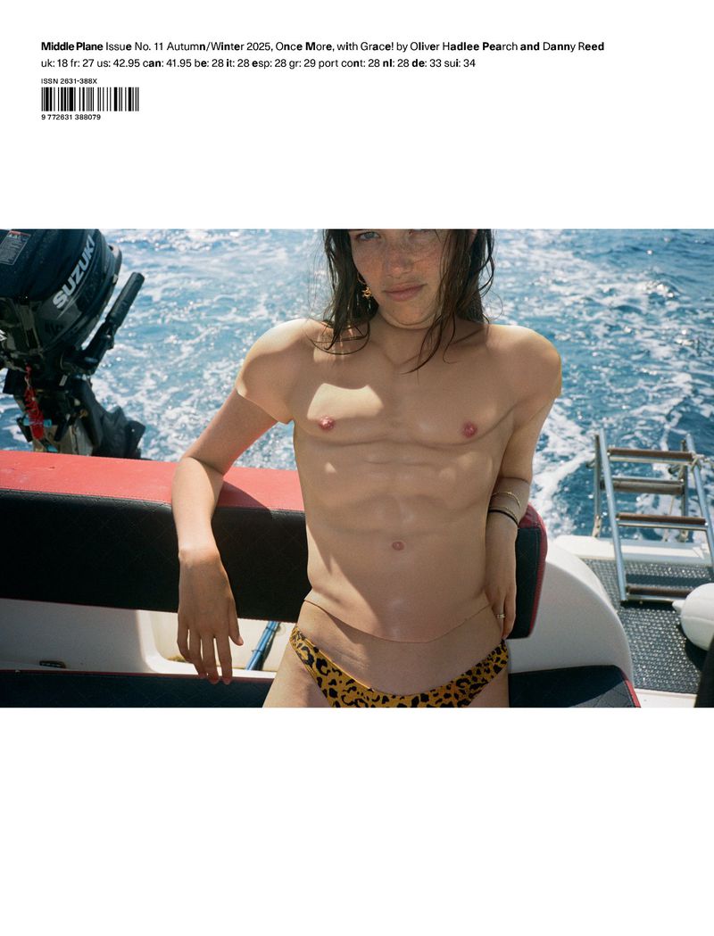 Topless young woman in leopard print bikini poses on boat in ocean. Fashion editorial shot in natural light.