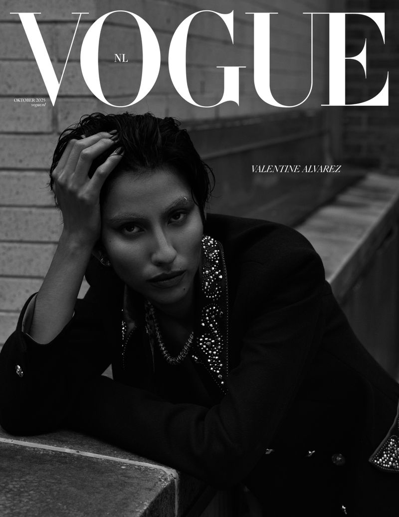 Vogue NL cover featuring a stylish person in a black embellished jacket, posed on steps with a brick wall backdrop, in monochrome.