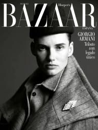 Close-up portrait of model Giedre Dukauskaite wearing a tailored grey coat and dark hat for Harper's Bazaar España.