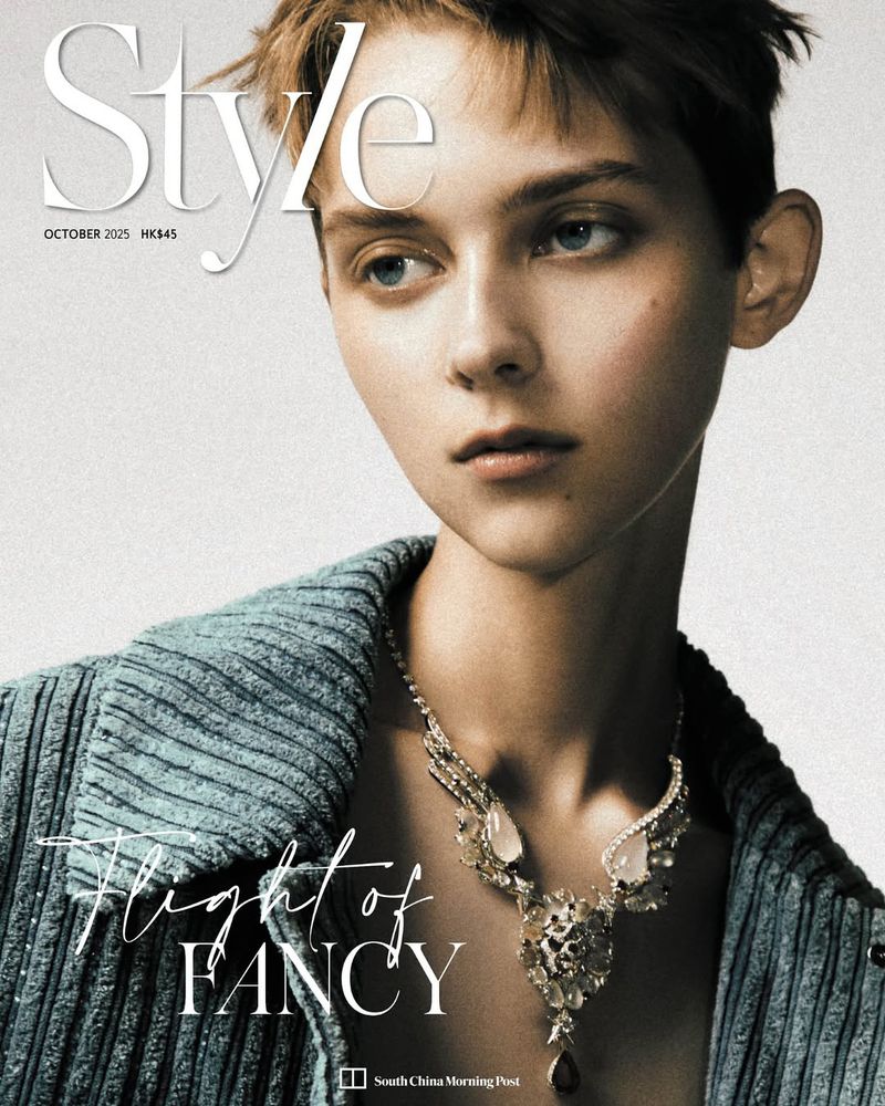 Magazine cover featuring a person with short brown hair wearing a blue jacket and ornate necklace against a neutral background.