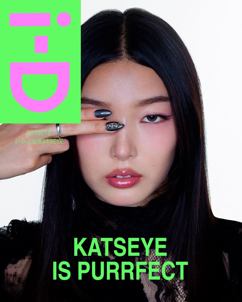 Close-up portrait of an Asian adult female with black hair partially covering her eye, makeup, and a pink and green logo graphic.
