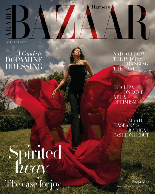 Harper's Bazaar cover featuring a model in a black outfit and a red flowing garment outdoors in a grassy setting on a sunny day.