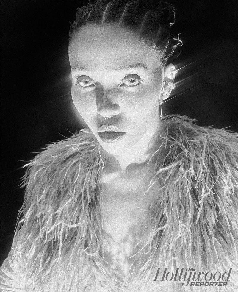 Striking black and white studio portrait of an adult female with braided hair and a feathered jacket looking intensely at the camera.