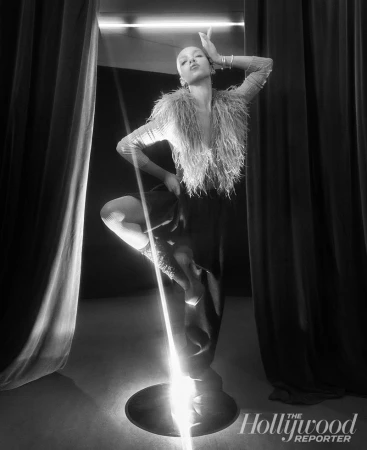 Black and white editorial portrait of FKA twigs posing between dark curtains illuminated by a vertical light bar.