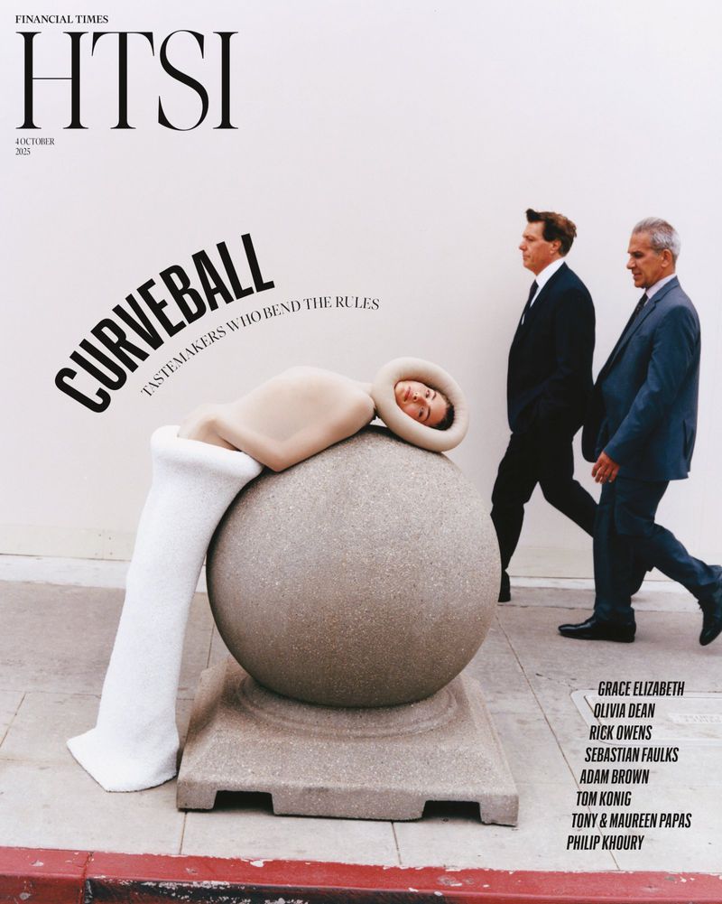 Magazine cover features woman in unique outfit reclining on a stone sphere, with two men in suits walking in the background on a sidewalk.