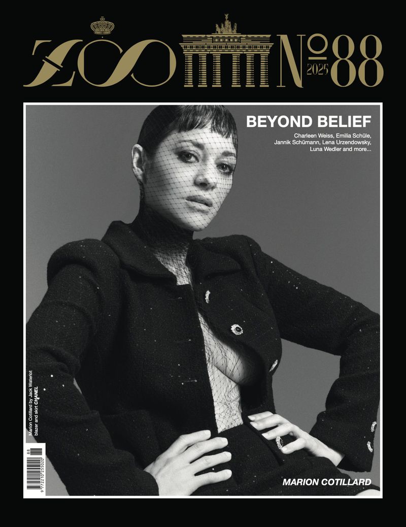 Black and white magazine cover featuring Marion Cotillard in a dark jacket and veil, against a grey background, with prominent text.
