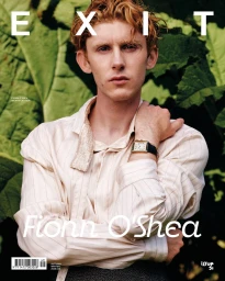 Fionn O'Shea wearing a striped cream shirt and gold watch in front of lush green foliage on an Exit Magazine cover.