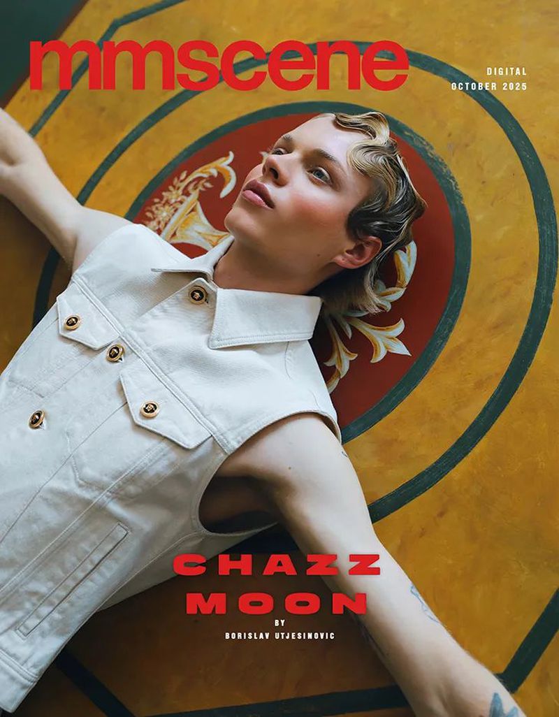 Magazine cover featuring a young adult male model with blond wavy hair and a sleeveless denim jacket, lying on a patterned surface.