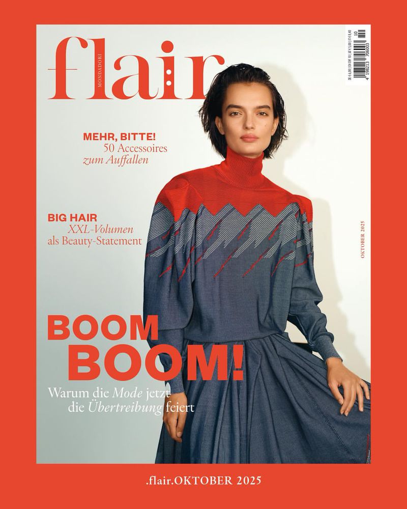 Magazine cover featuring a model with short dark hair wearing a red and gray long-sleeve dress against a light background and red border.