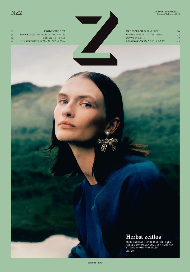 Fashion magazine cover featuring a portrait of a brunette woman with a gold bow earring against a soft, blurred mountain backdrop.