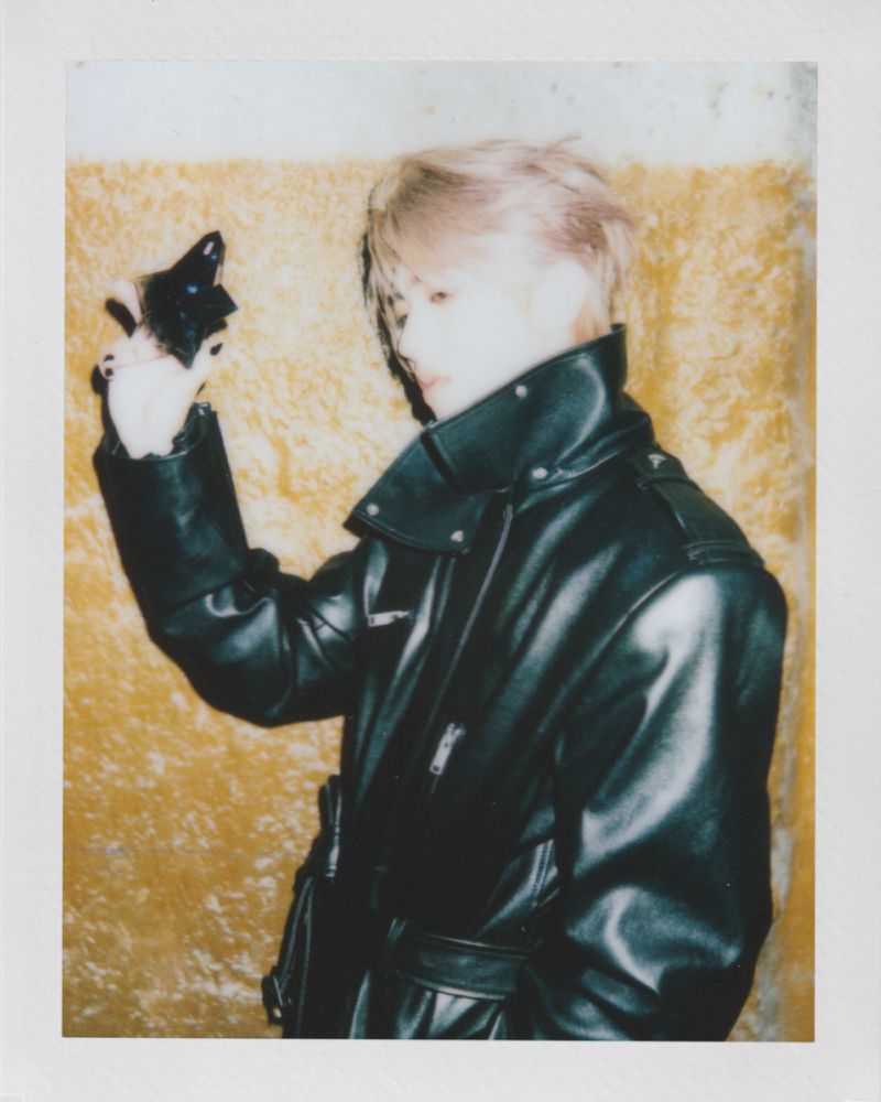 Close-up portrait of a person with light hair and a black leather jacket against a blurred background with a vintage aesthetic.