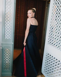 Amanda Seyfried looking over her shoulder in a strapless dark navy Prada evening gown with a bold red stripe.
