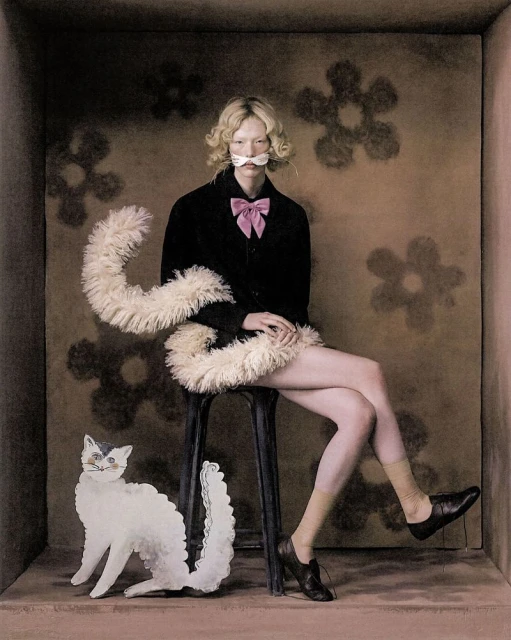 A person sits on a stool in a vintage-styled photo studio with a cat cutout and flower-patterned wallpaper, creating a whimsical atmosphere.