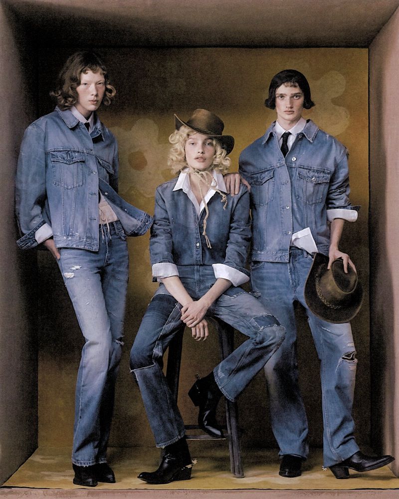 Three people in denim outfits pose indoors against a neutral backdrop with floral design, showcasing fashion and contemporary style.