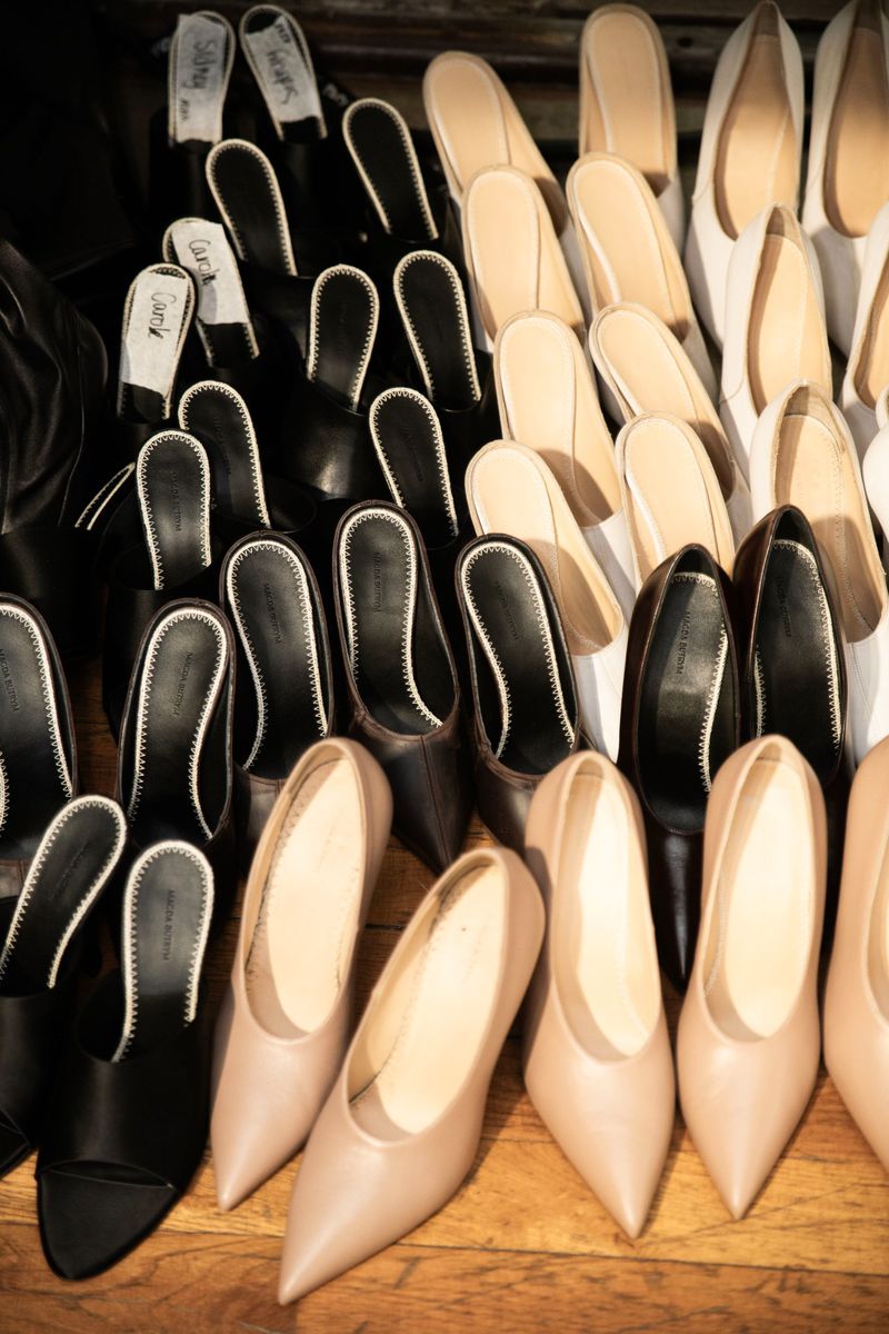Rows of black, beige, and white heeled shoes, closely arranged. Women's fashion footwear on a wooden floor, commercial product showcase.