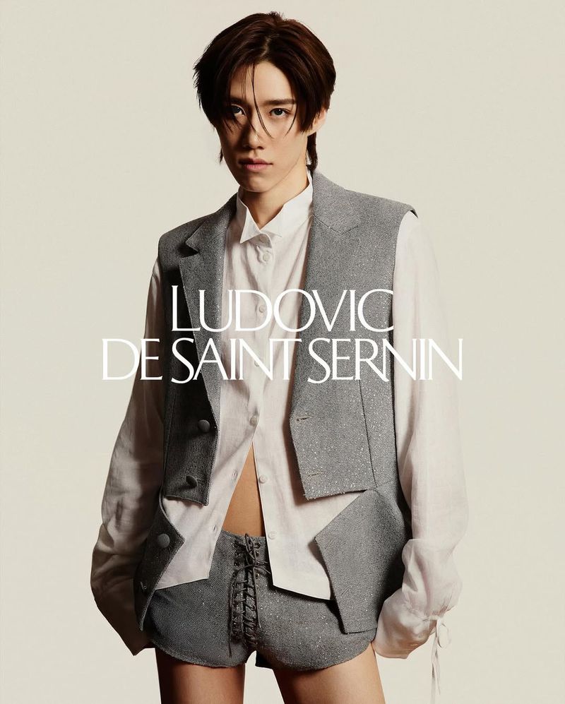 Fashion shot of a young adult in a vest and shorts, posing in front of a neutral backdrop with the brand name LUDOVIC DE SAINT SERNIN.