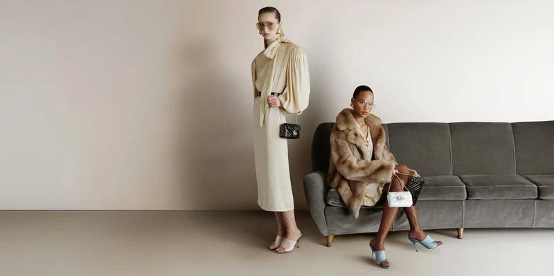 Two female models posing with designer handbags against a grey sofa and neutral studio wall for Gucci FW25 digital campaign.