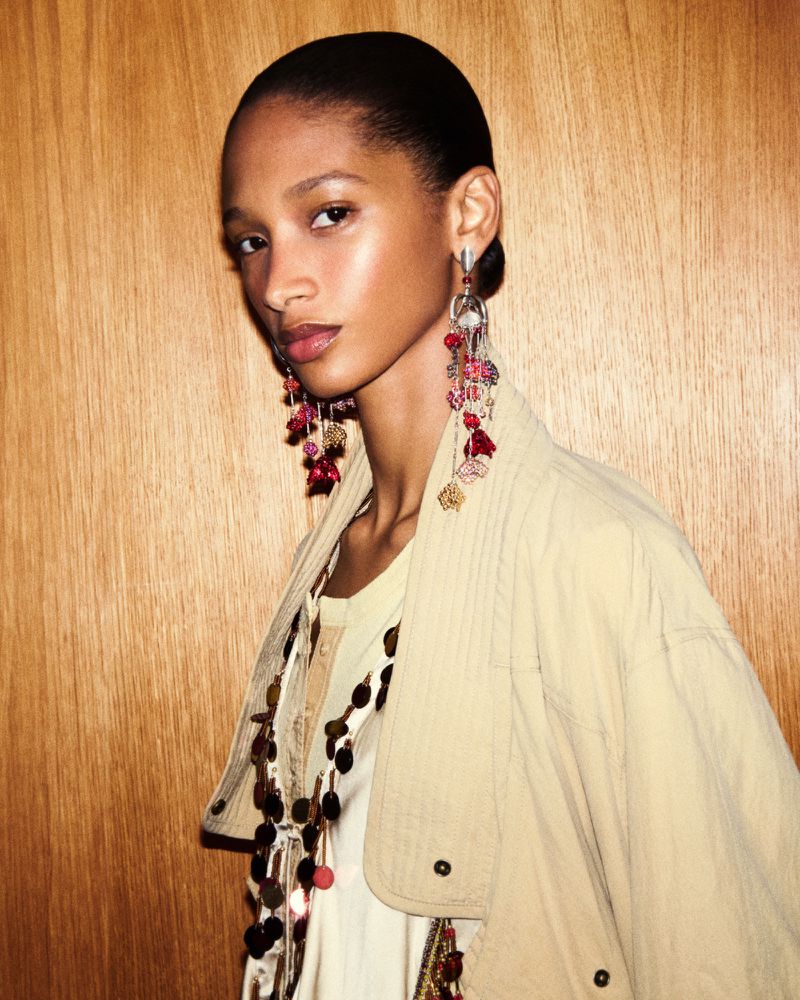 Portrait of an adult female wearing dangly earrings and a beige jacket against a wood background. Beauty and fashion concept.