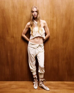Model wearing cream knit halter top and loose trousers against wood paneling