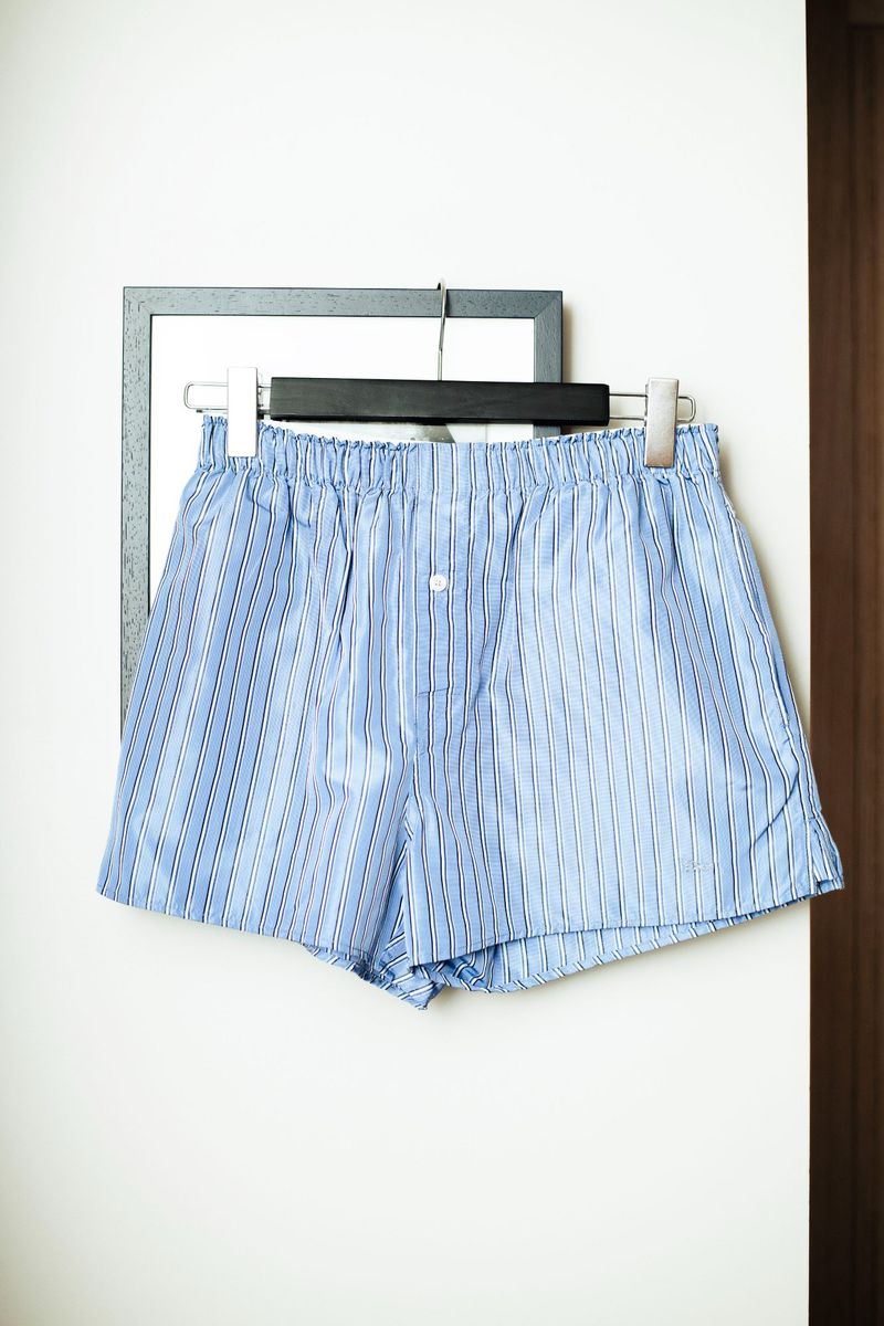 Blue and white striped boxer shorts hang on a hanger against a white wall with a gray framed picture for a clean, minimal look.